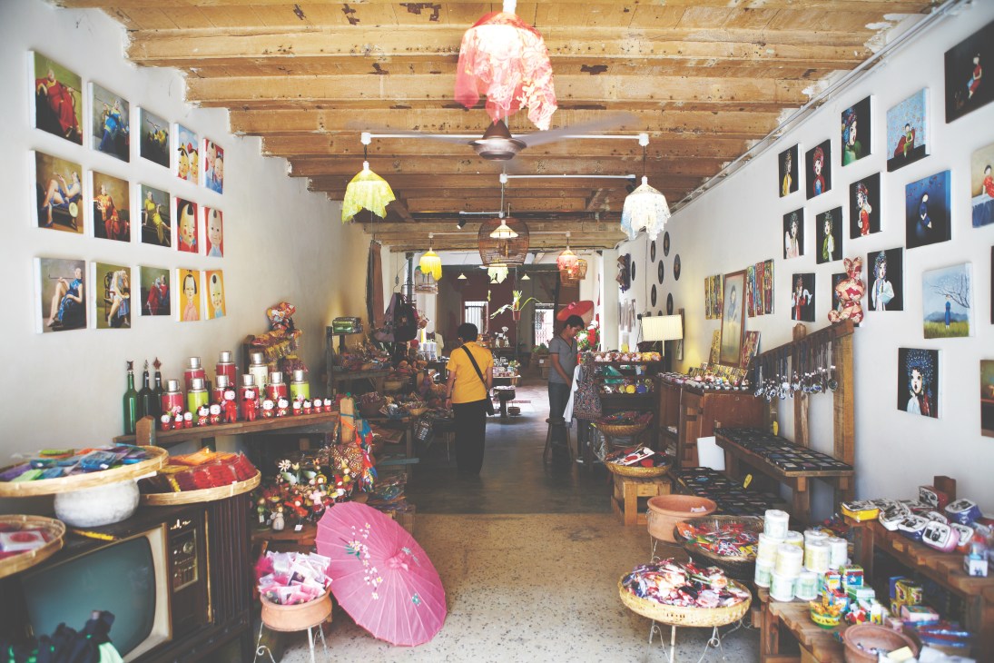Interior of a traditional shop in George Town displaying colorful merchandise including umbrellas, artwork, and decorative items on wooden shelves.