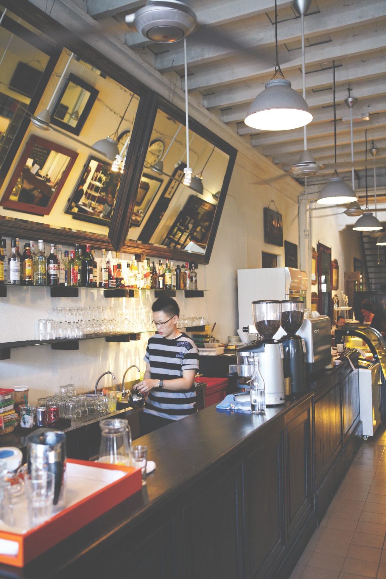 Bartender in striped shirt working at China House bar with pendant lights and shelving.