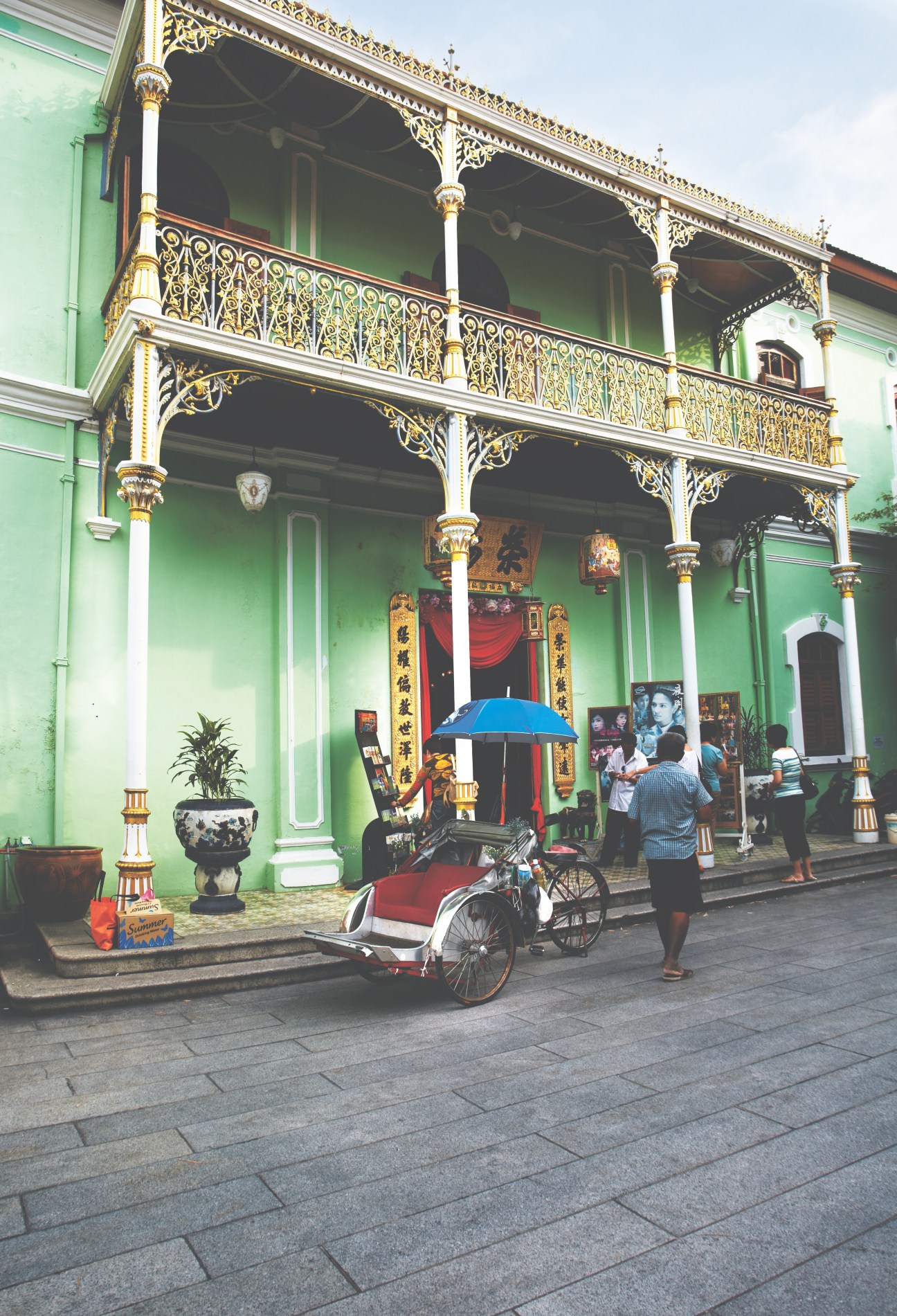 Green colonial building with ornate gold railings, white columns, and Asian architectural details in George Town.
