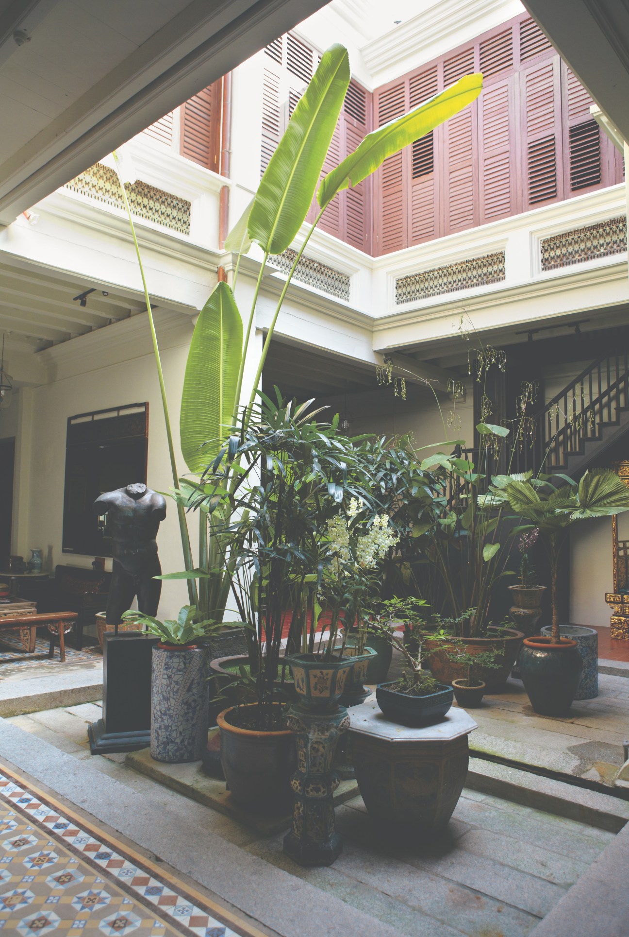 Leafy courtyard of a traditional George Town house with potted plants and open roof.