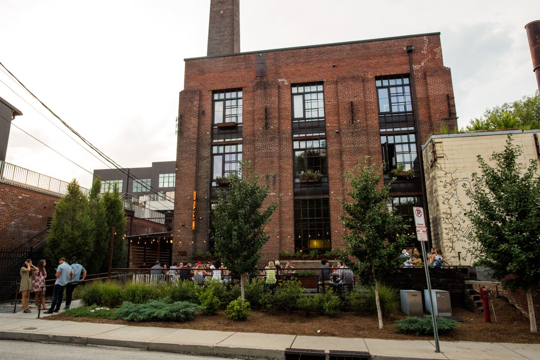 Converted industrial brick building with large windows and outdoor seating area surrounded by greenery in Germantown.