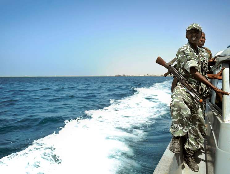 Armed Somali coast guard officer in camouflage uniform standing on patrol boat in Indian Ocean waters.