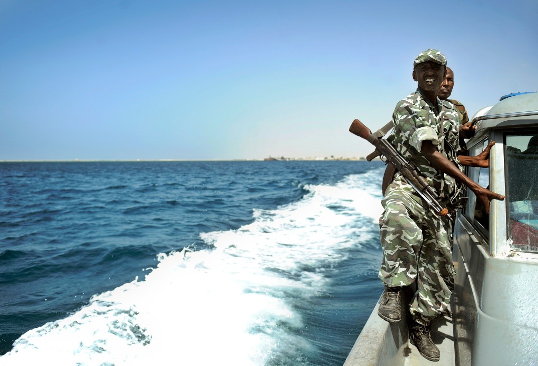 Armed Somali coast guard officer in camouflage uniform standing on patrol boat in Indian Ocean waters.