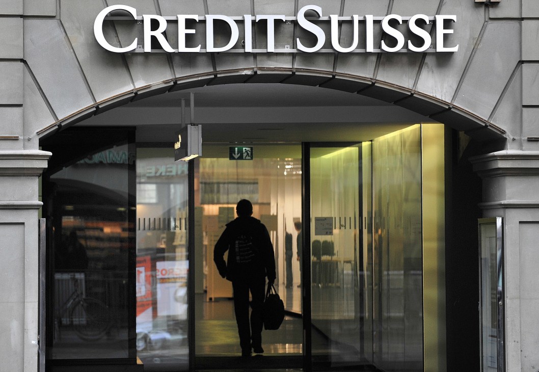 Person entering a Credit Suisse bank branch through glass doors with illuminated signage above.