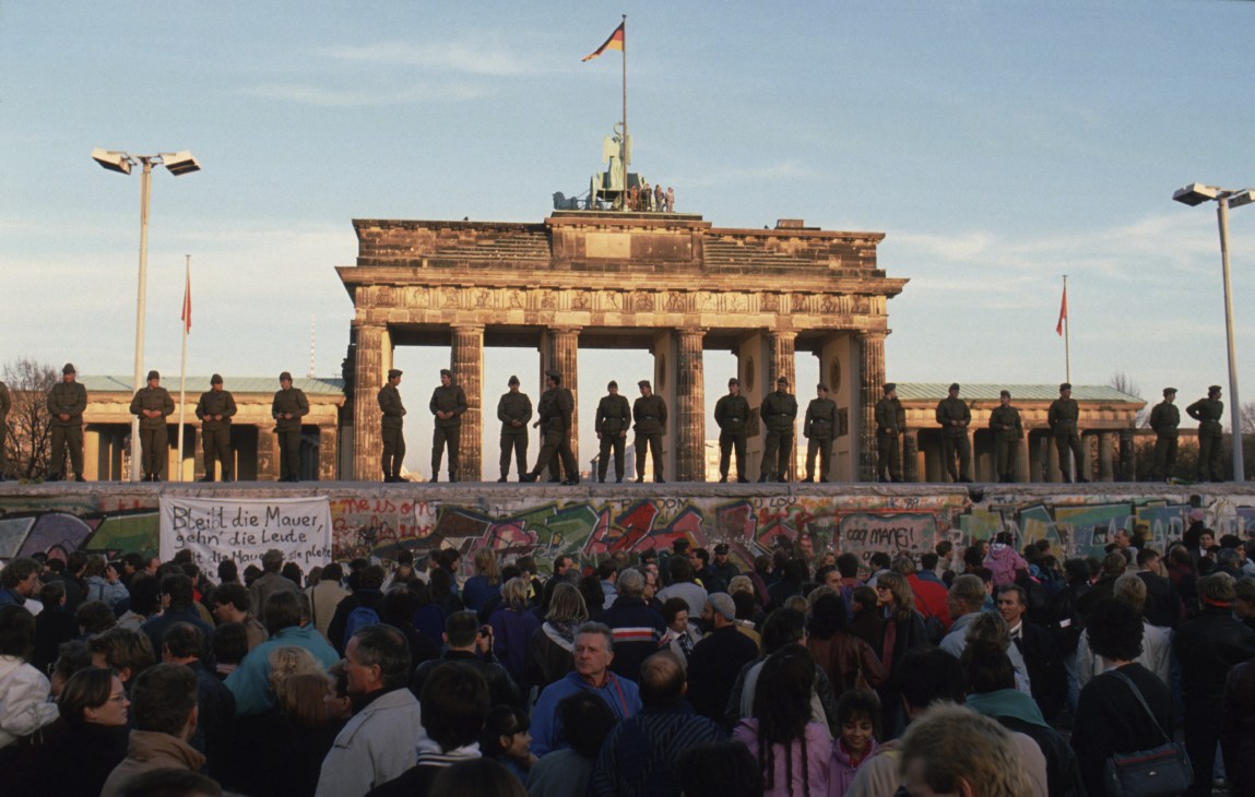 Border guards standing at Brandenburg Gate as crowds gather below the fallen Berlin Wall on November 9, 1989.
