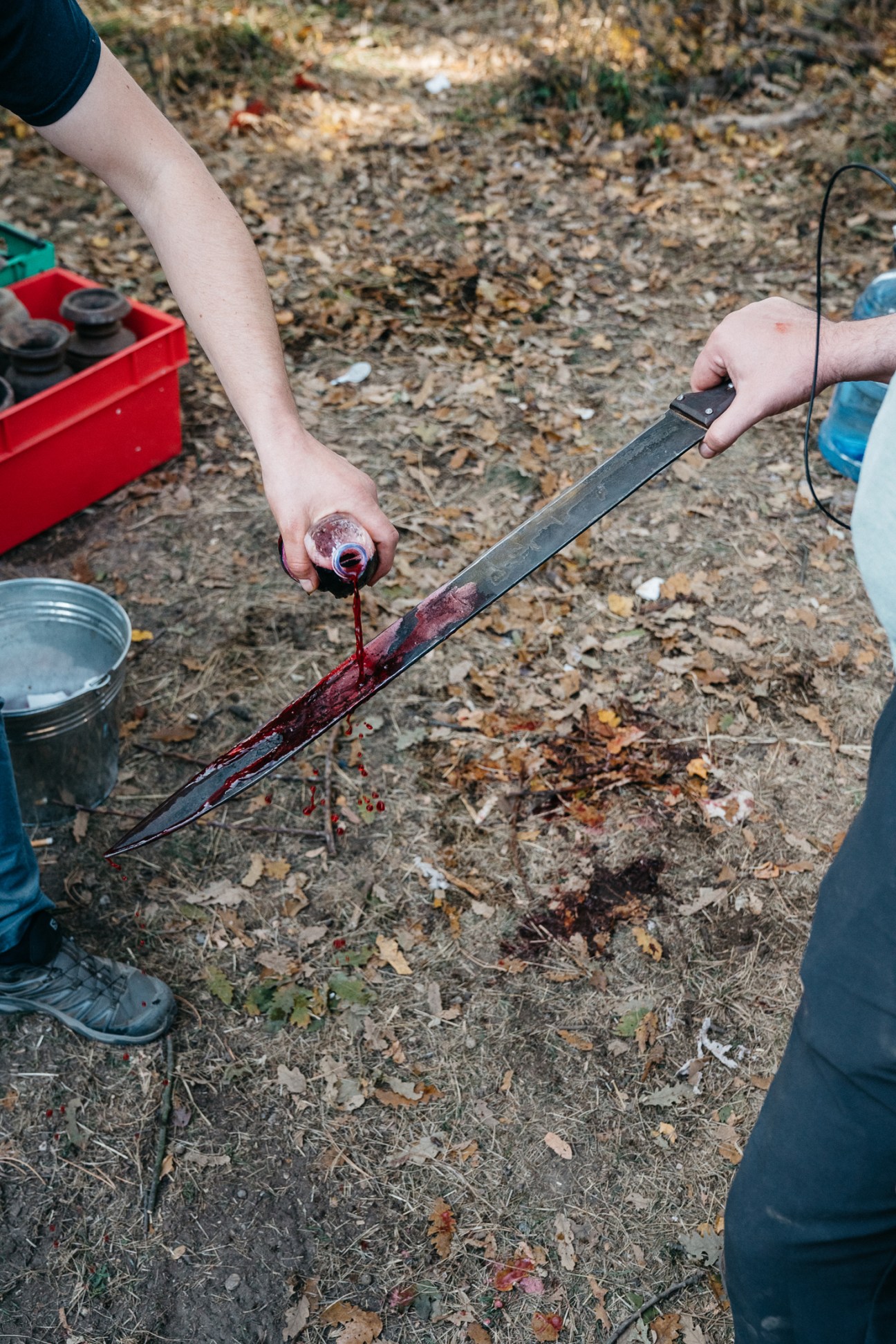 Hands applying fake blood to a sword prop on the ground during The Barbarians filming.
