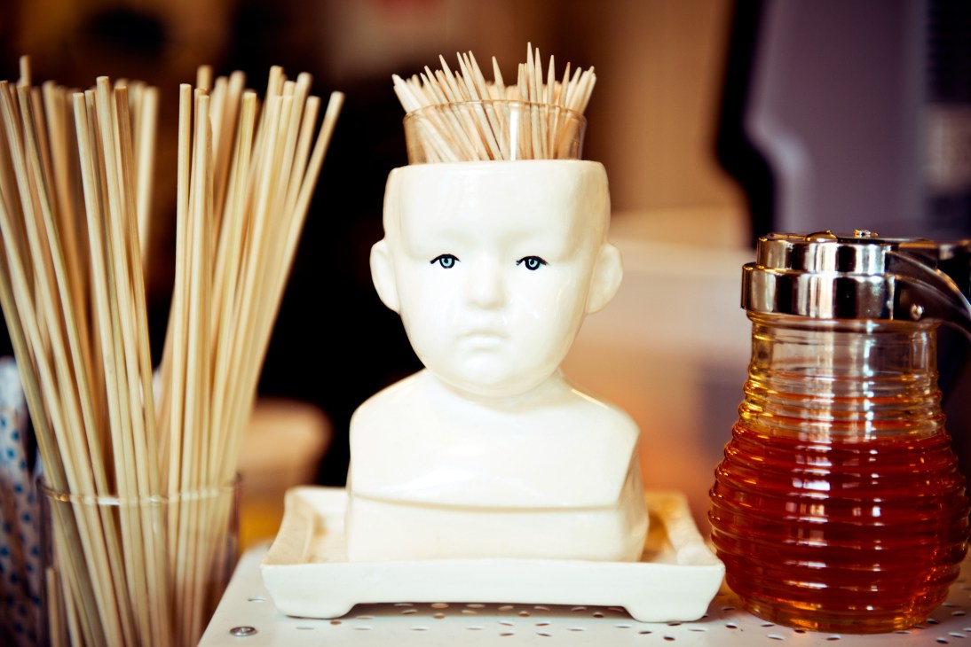 White porcelain bust head with toothpicks inserted on top, flanked by a container of toothpicks and an amber glass dispenser.