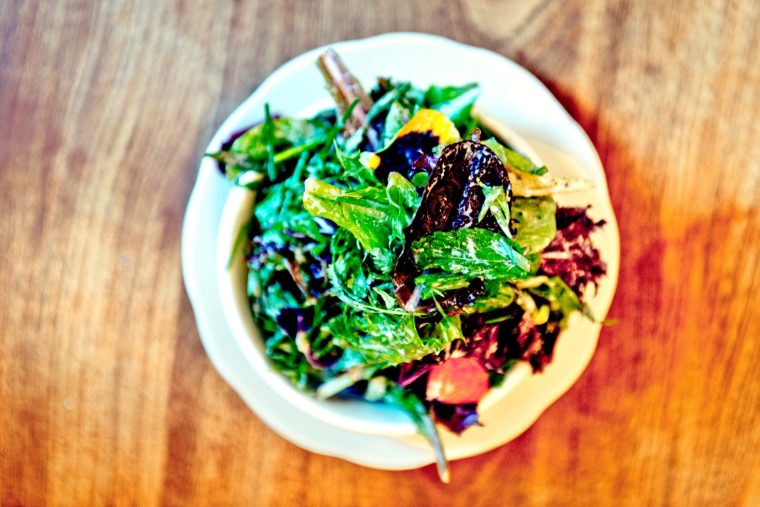 Herb salad with chives, mint, parsley, buttermilk dressing and pansies on a white plate.