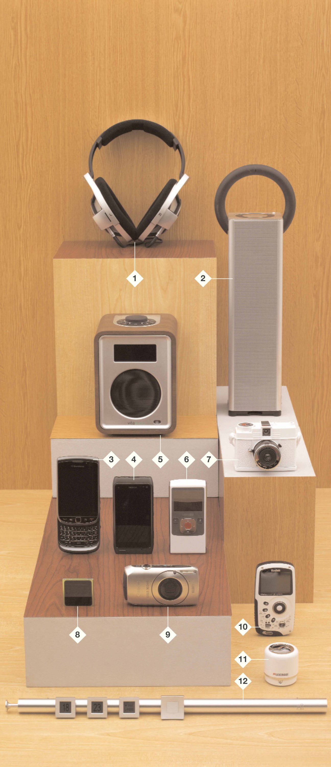 Technology gift items arranged on wooden display blocks including headphones, speakers, phones, cameras and accessories.