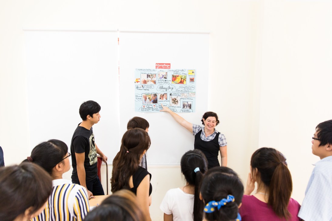 Teacher Alex Menties points to a German language and culture poster while Vietnamese nursing students listen in a Hanoi classroom.