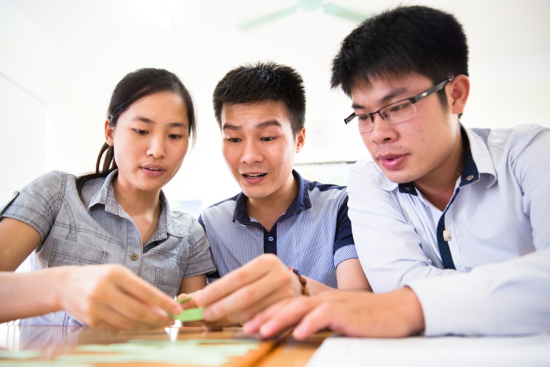 Three Vietnamese nursing students studying German grammar with flashcards during language training in Hanoi.