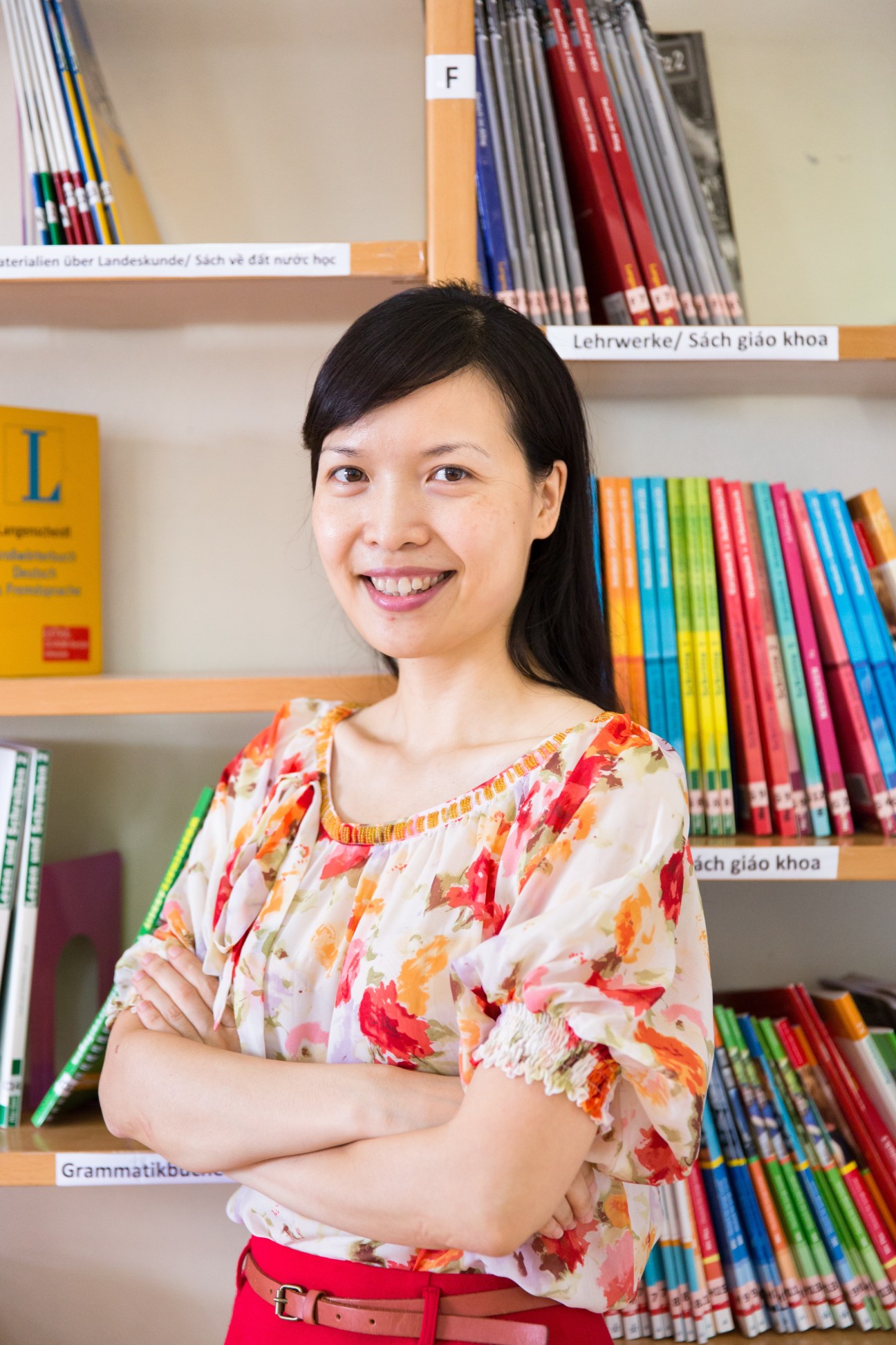Teacher Nguyen Thi Thu Huong smiles at the camera in front of shelves of German language learning materials.
