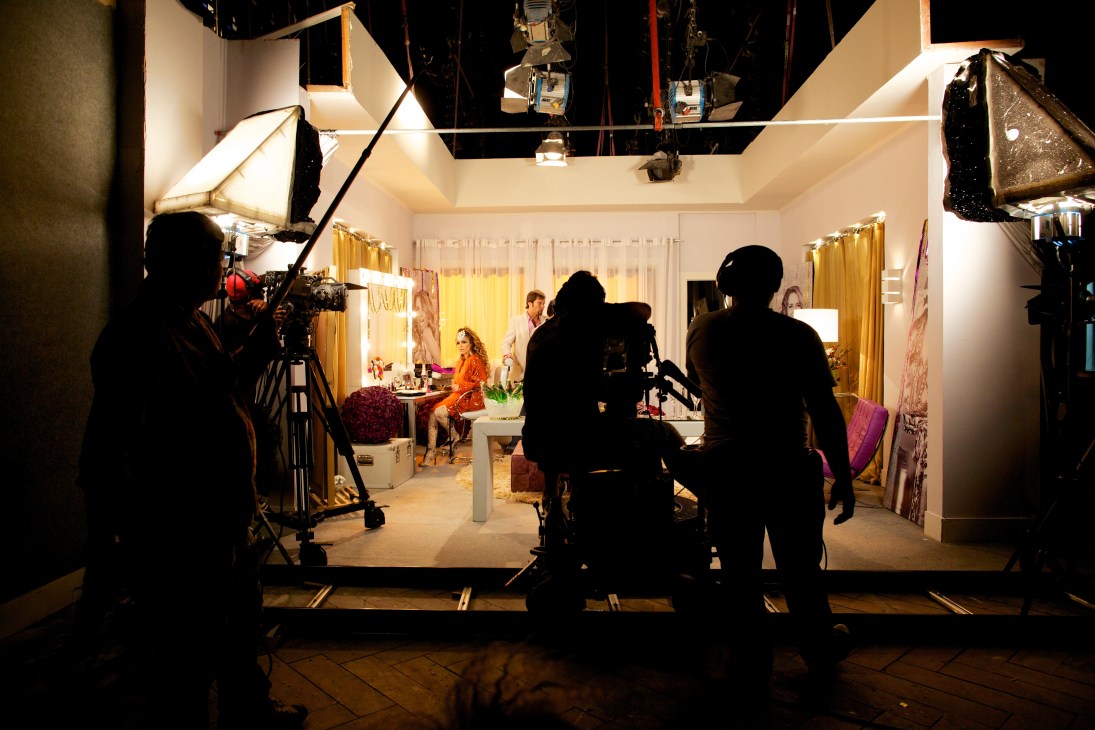 Camera crew filming a scene on a Brazilian telenovela set with actors and bright studio lighting.