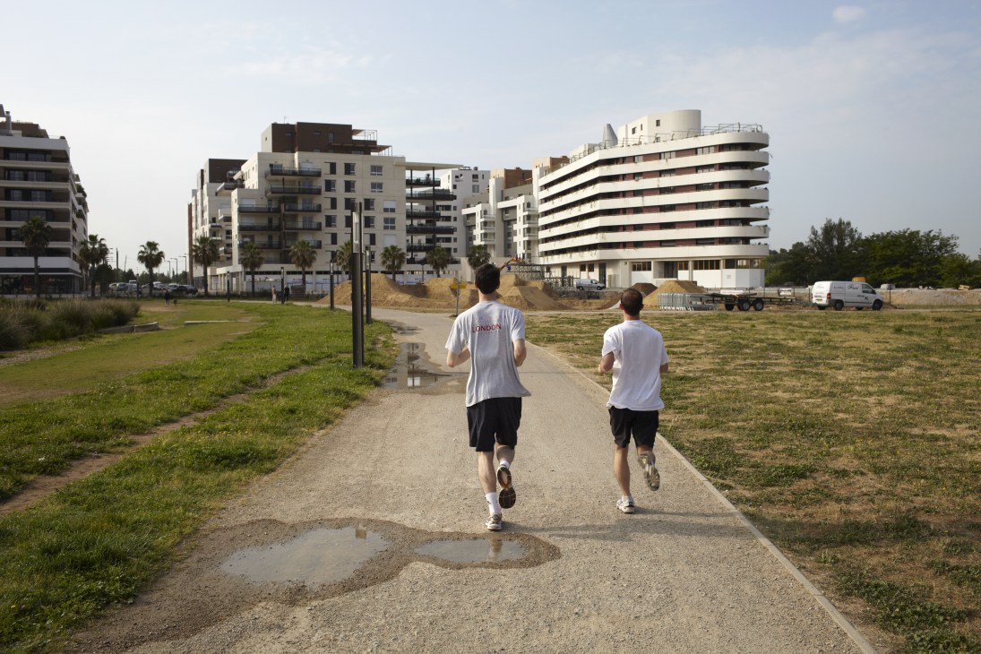 Two joggers running on a path in the Port Marianne district with modern residential buildings in the background.