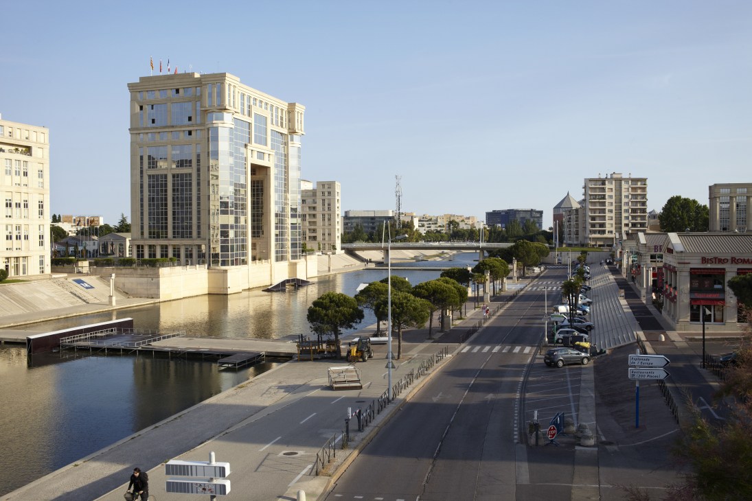 Modern beige building with flags on waterfront in Montpellier's Antigone business district