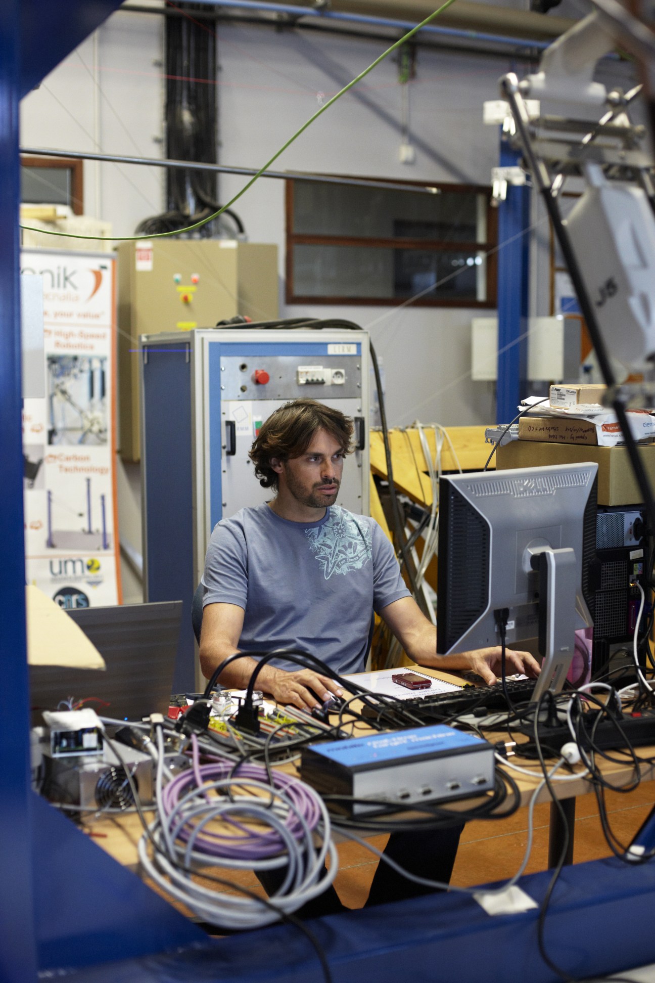 Micaël Michelin works at a computer in Tecnalia's robotics laboratory surrounded by equipment and cables.
