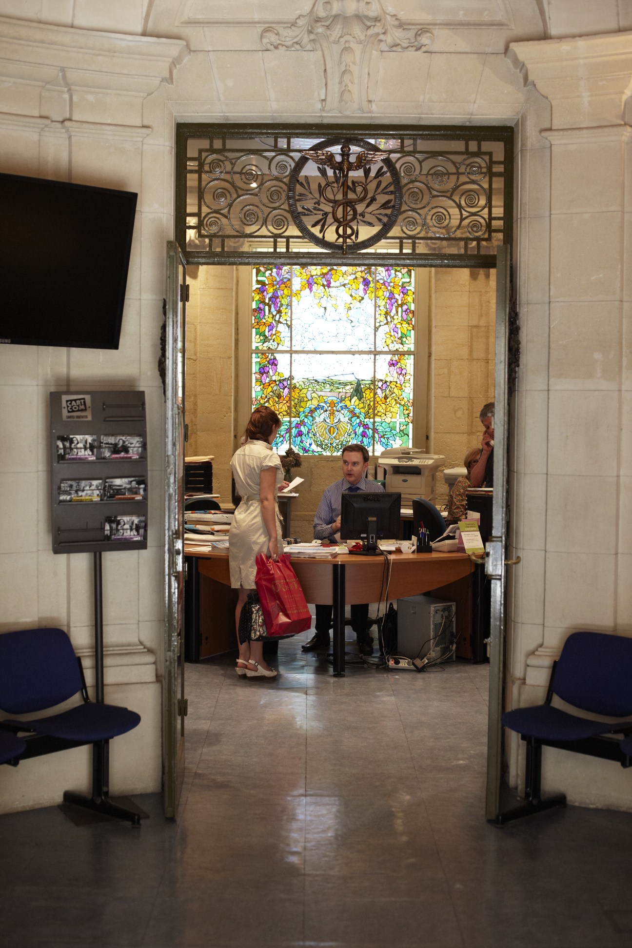 Chamber of Commerce reception desk in ornate sandstone building with decorative ironwork above the doorway and stained-glass window.
