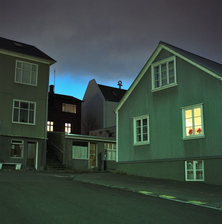 Illuminated green and black corrugated metal houses on a Reykjavik side street at dusk.