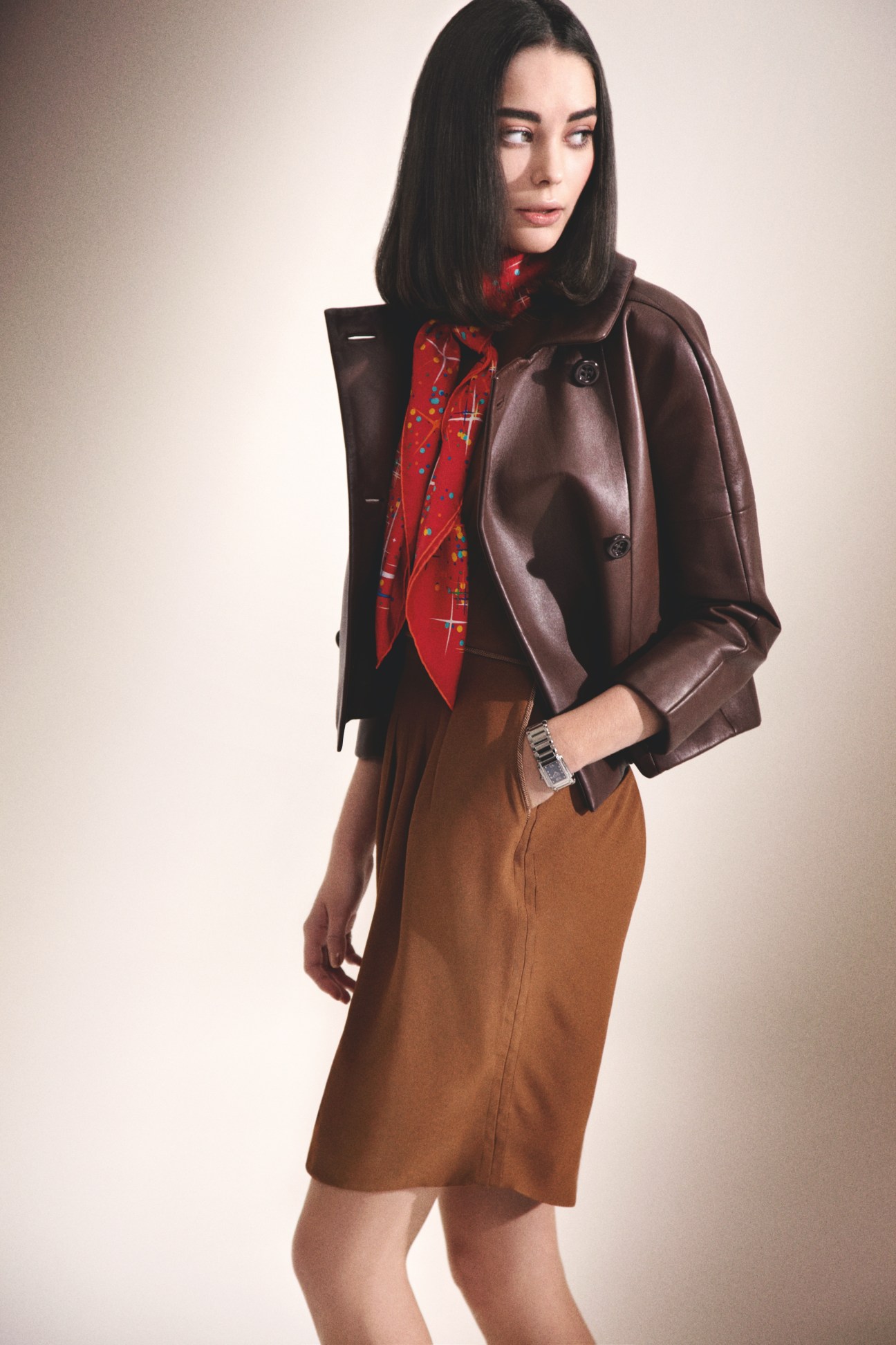 Model wearing a brown Loewe jacket, red Hermès scarf, camel Azzaro dress, and Patek Philippe watch.