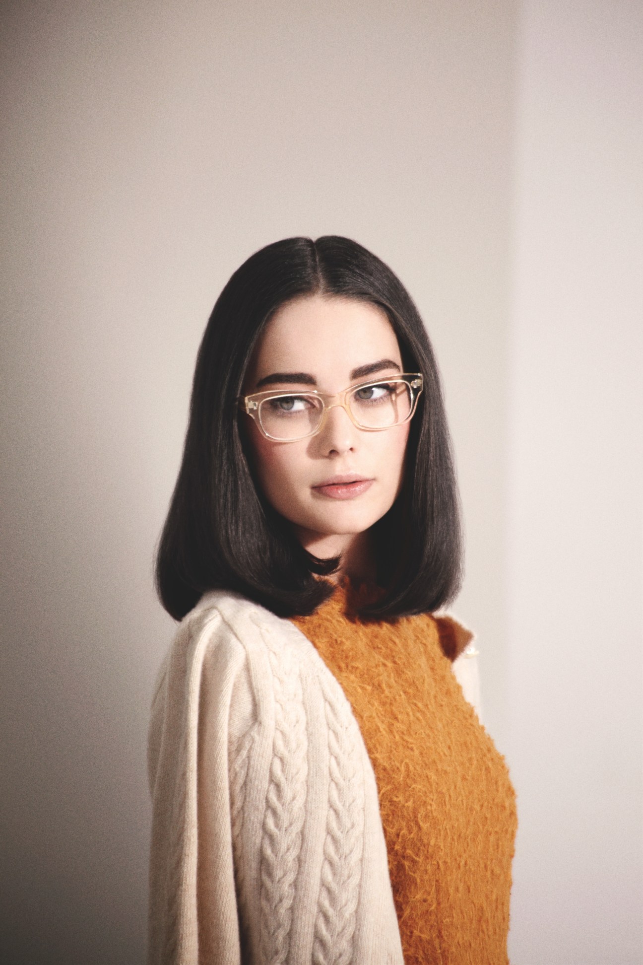 Model wearing Oliver Peoples glasses, Bottega Veneta dress, and Maison Kitsuné cardigan in golden brown tones.