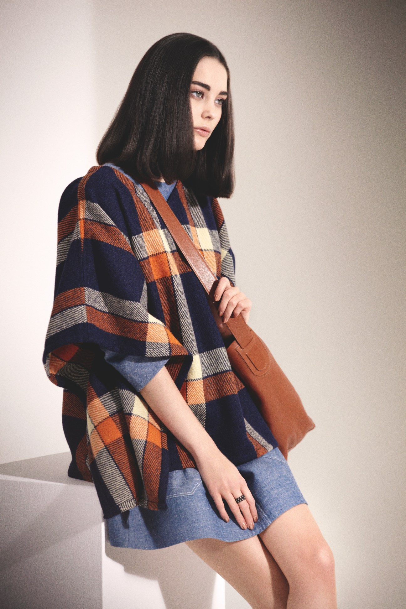 Model wearing A.P.C. cape, G-Star dress, Delvaux bag and Bottega Veneta ring against neutral background.