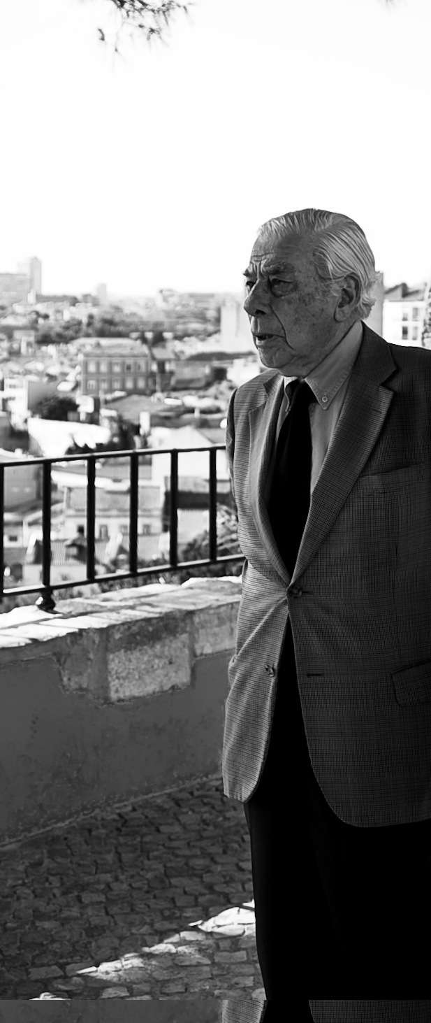 Black and white portrait of Gonçalo Ribeiro Telles on a balcony overlooking Lisbon cityscape.