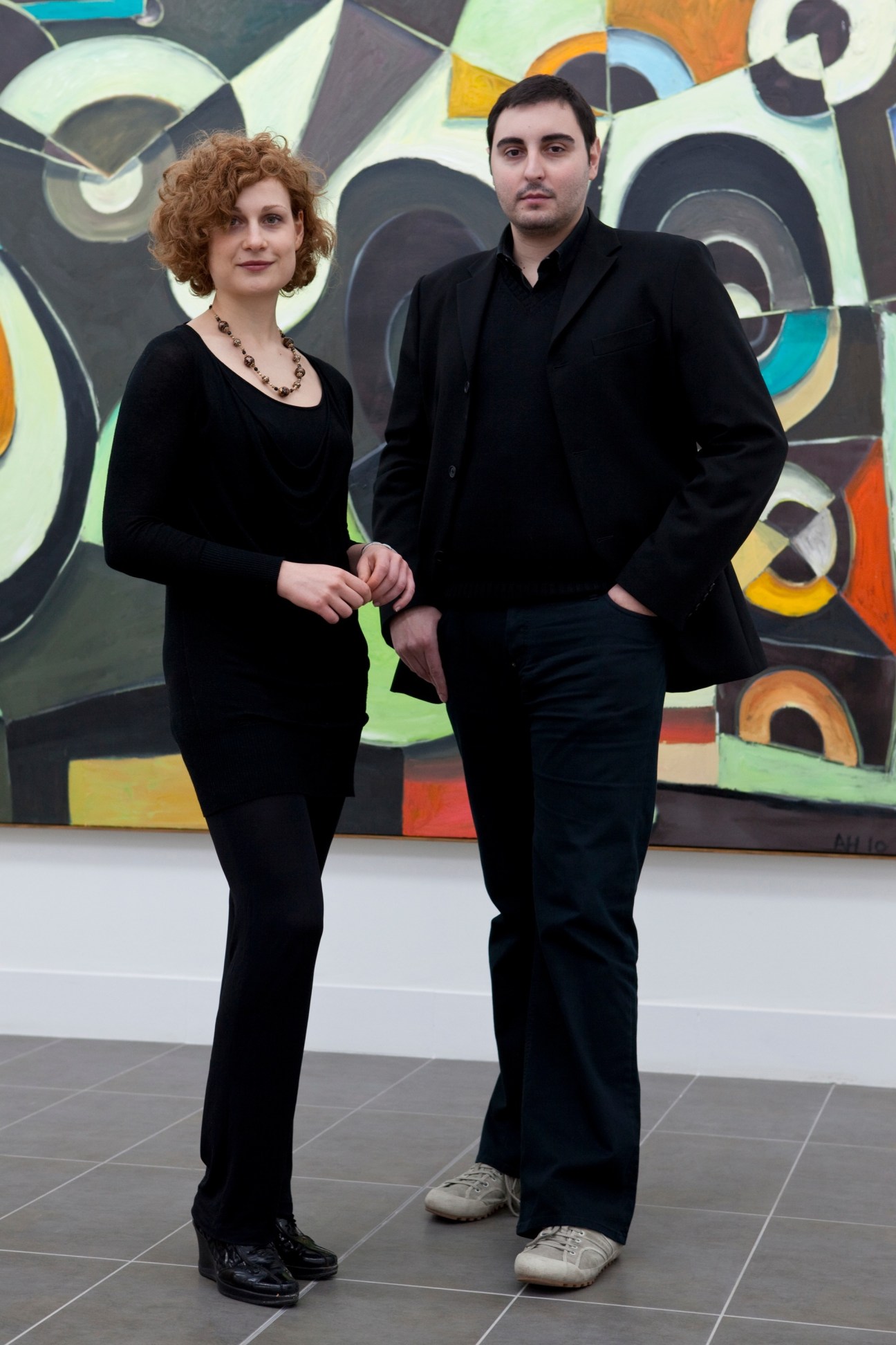 Two people stand in front of a colorful abstract artwork in a modern gallery space.