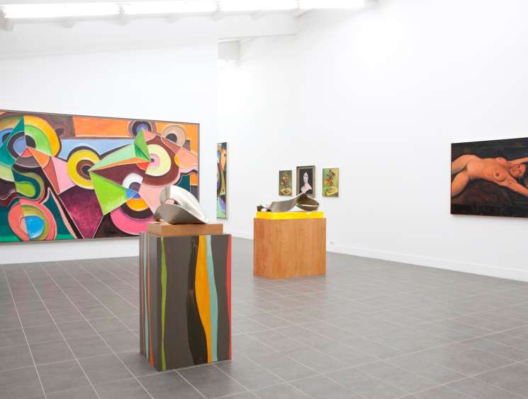 Contemporary art gallery interior with colorful abstract painting, sculptural pedestals, and figurative artworks on white walls.