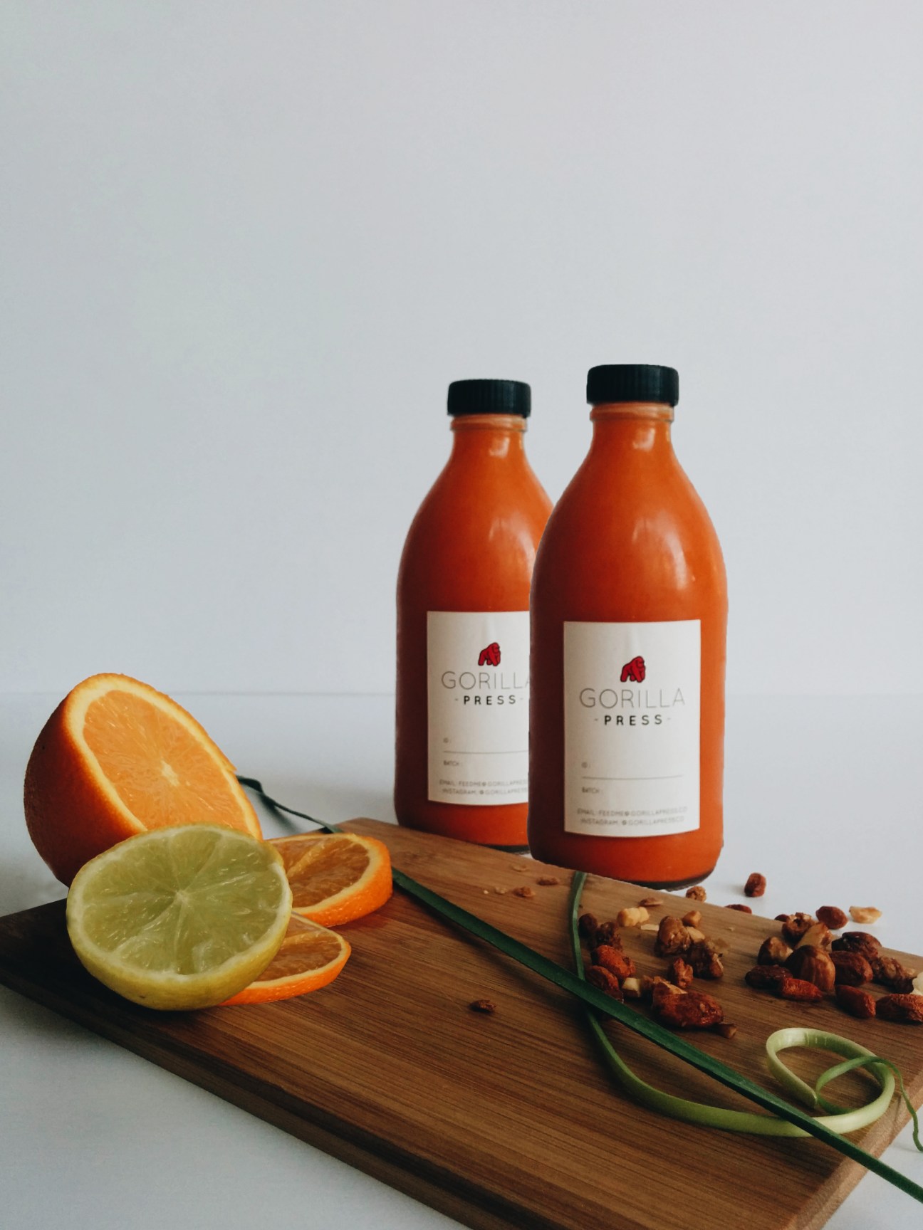 Two Gorilla Press bottles of orange juice with fresh citrus slices and ginger on a wooden board.