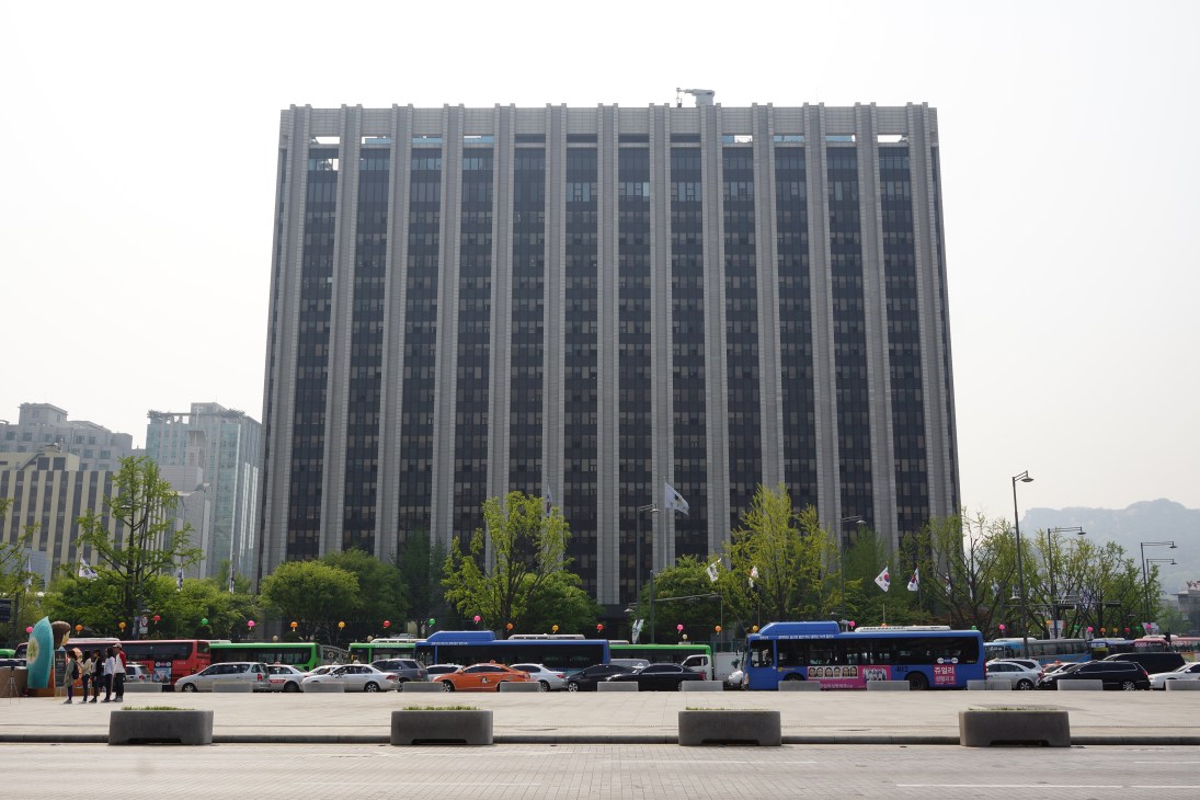 Large government building with vertical ribbed facade and parked vehicles in front, Seoul.