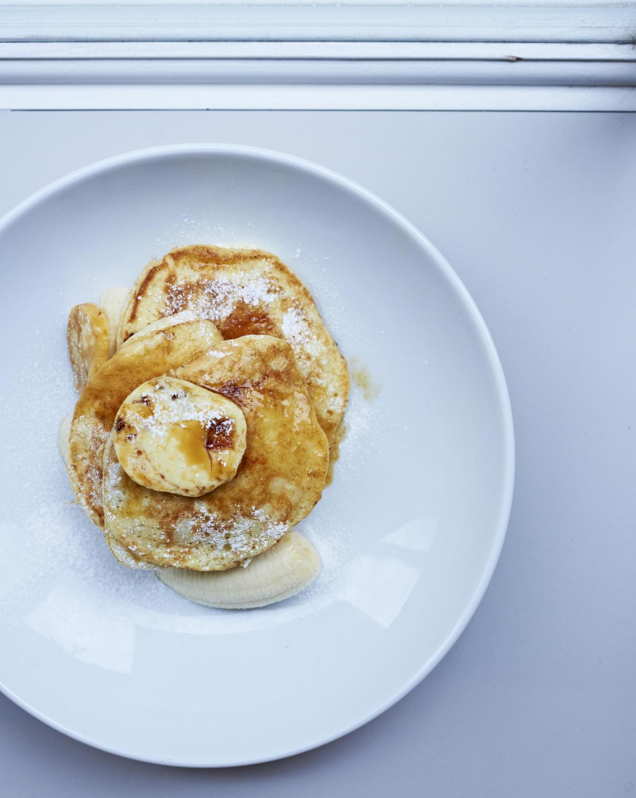 Fluffy pancakes dusted with powdered sugar served on a white plate with sliced banana.