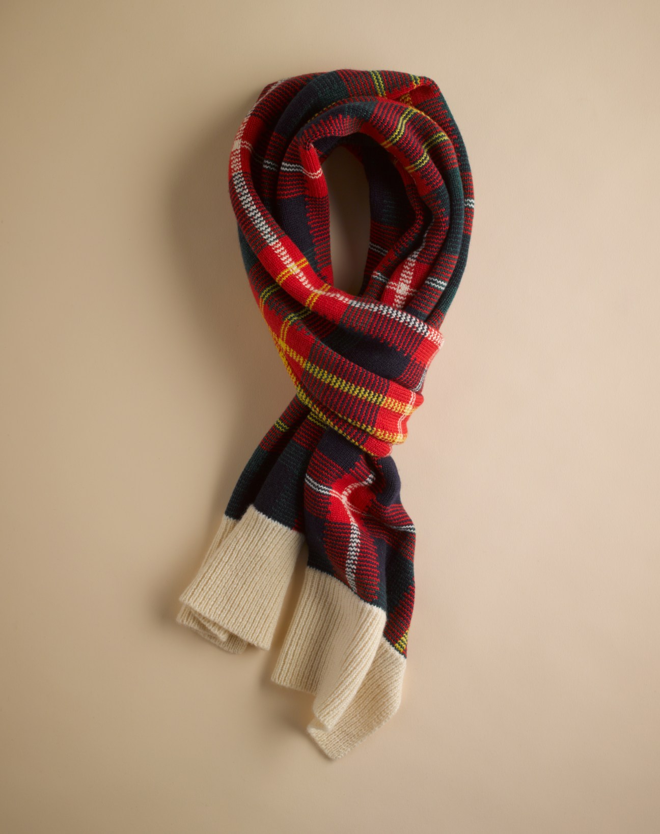 Red and navy tartan scarf with cream ribbed cuff against beige background.