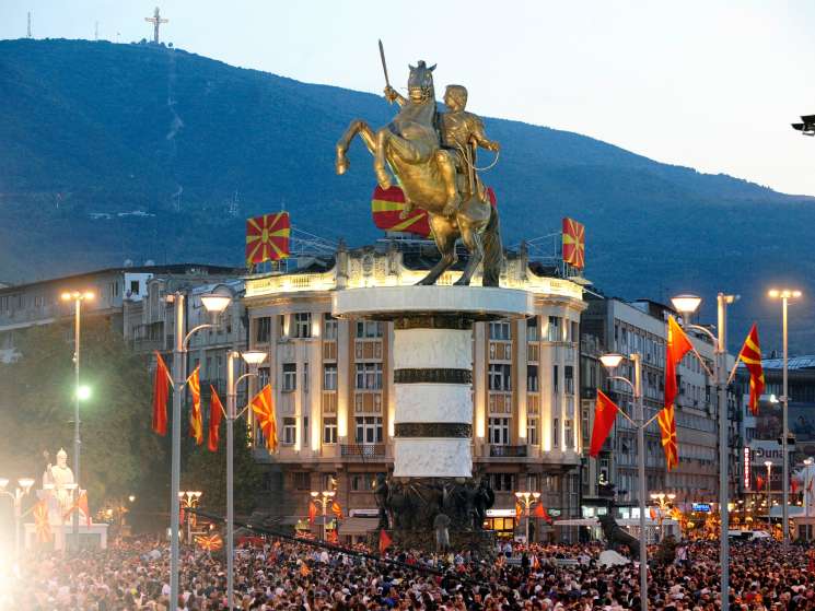 Bronze statue of Alexander the Great on horseback in Skopje's central square, surrounded by Macedonian flags and crowds.