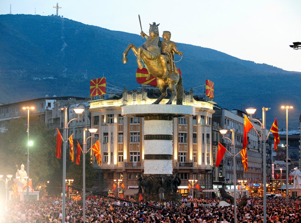 Bronze statue of Alexander the Great on horseback in Skopje's central square, surrounded by Macedonian flags and crowds.