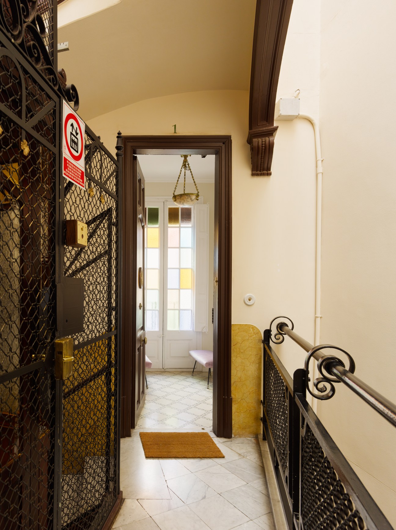 Interior hallway with cream walls, ornate dark brown door frame, decorative iron railings, and pendant light fixture.