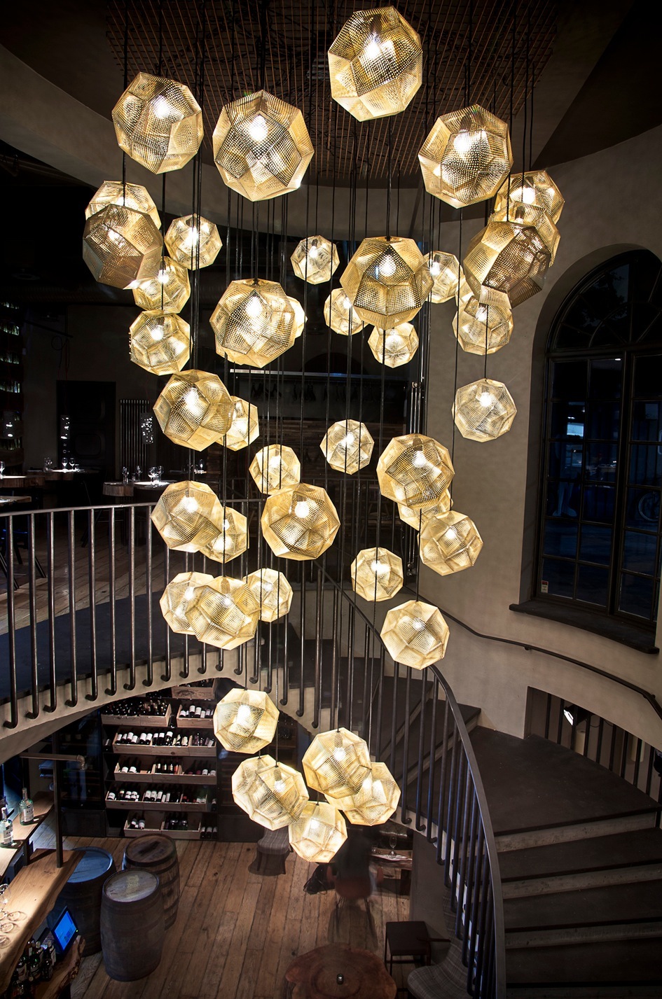 Interior view of Grill Market restaurant in Reykjavik showing hanging geometric gold pendant lights above a wooden staircase and dining area.
