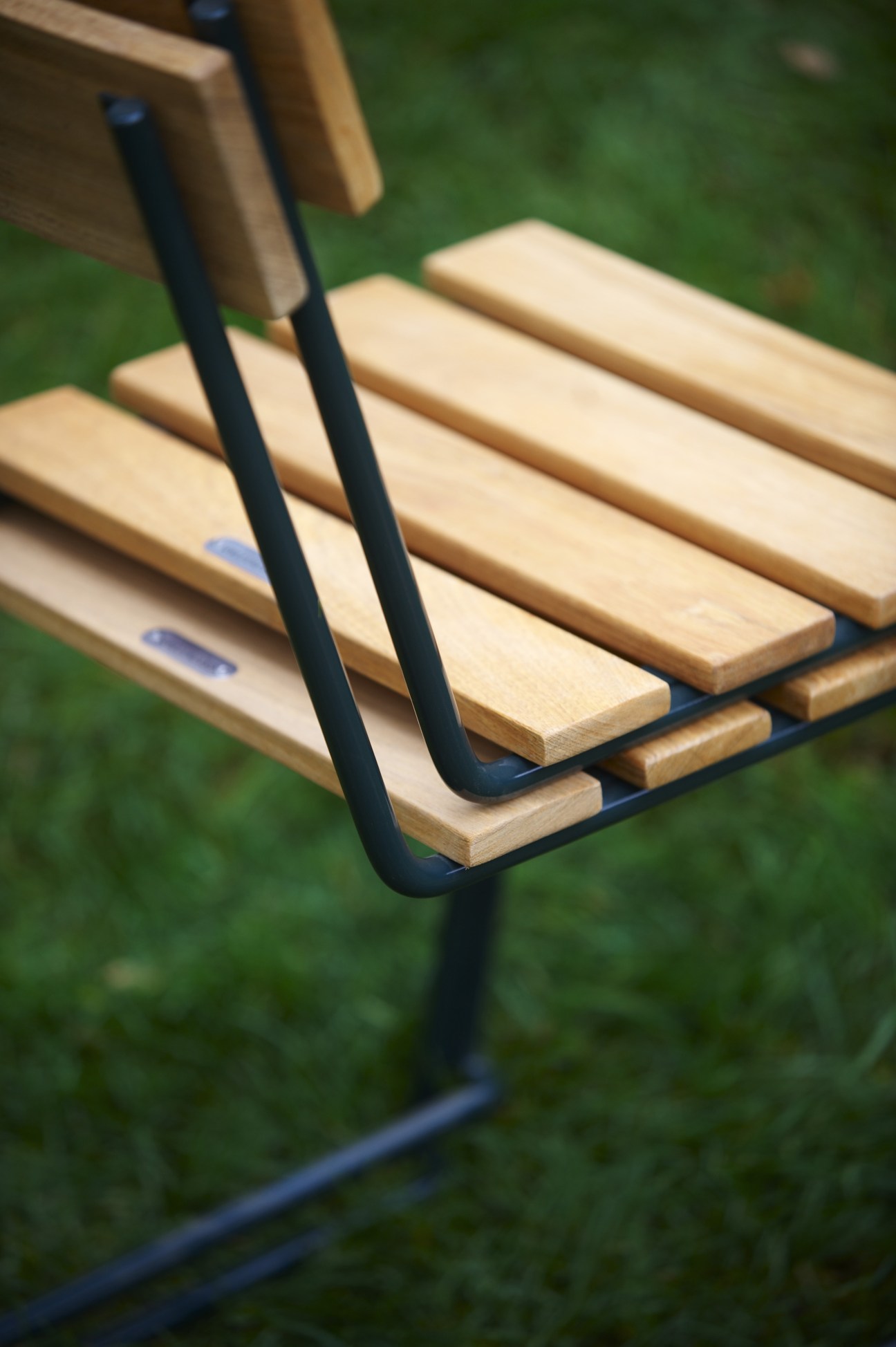 Close-up detail of Chair 1 by Grythyttan Stålmöbler showing wooden slats and black metal frame against grass background.