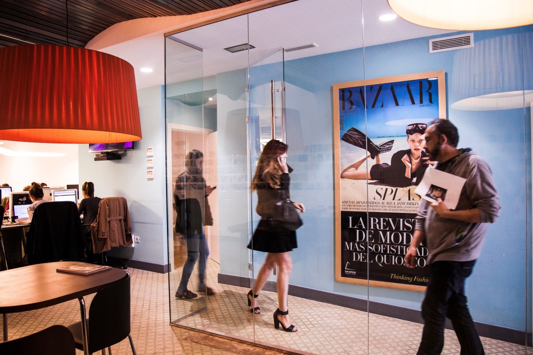 SpainMedia office interior in Madrid showing glass partitions, blue walls, Harper's Bazaar poster, and employees working at desks.