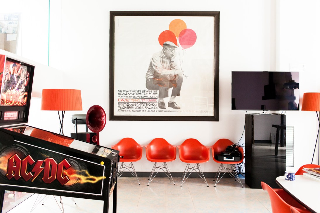 Modern office workspace with red chairs, colorful artwork featuring balloons, and contemporary furnishings against white walls.