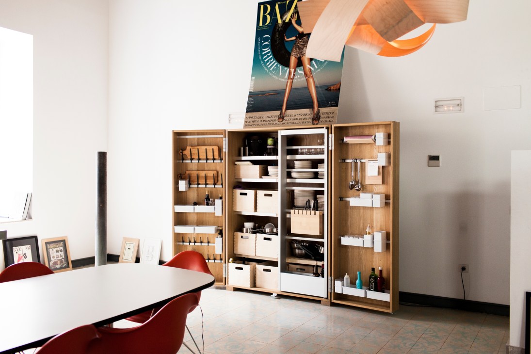 Modern office interior with wooden storage cabinets, red chair, white desk, and magazine poster on white wall.