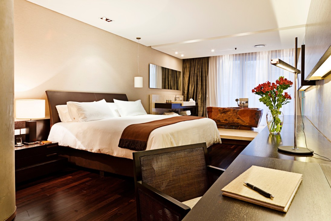 Modern luxury hotel bedroom with brown upholstered bed, white linens, dark wood flooring, and contemporary furnishings at Chateau Mio Buenos Aires.