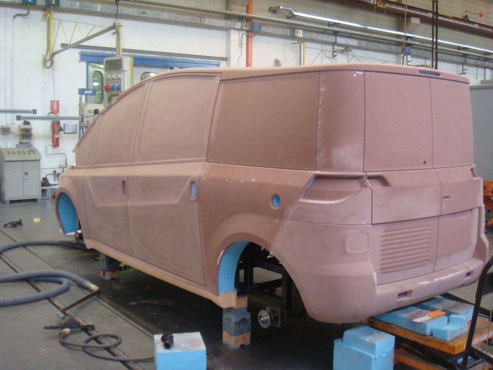 Clay model of Karsan V-1 taxi prototype in factory workshop with blue wheels.