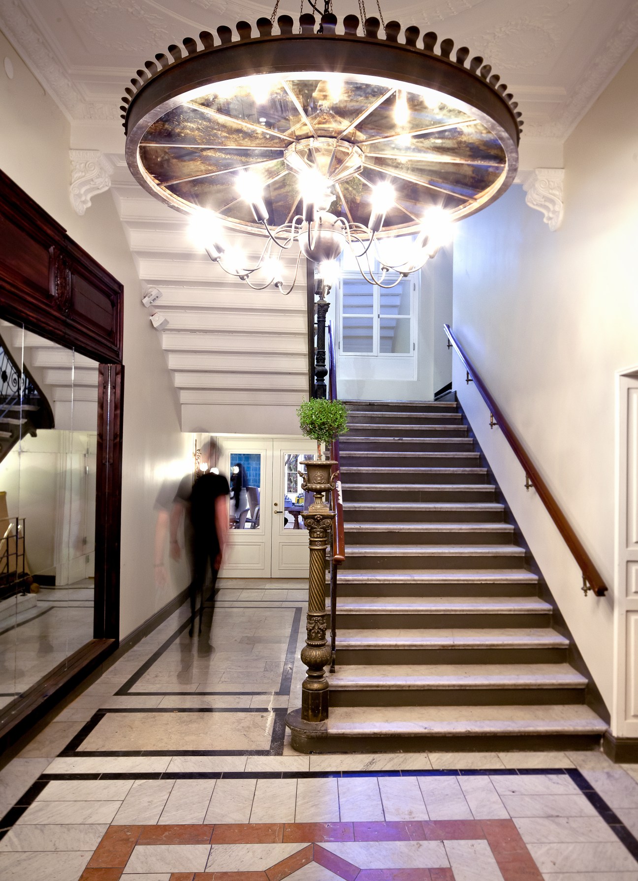Elegant hallway with ornate chandelier, staircase and decorative floor at Nosh and Chow Stockholm restaurant.