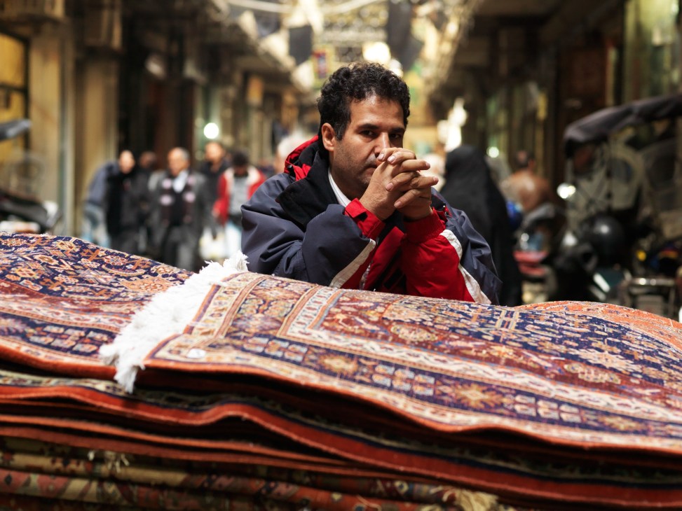 A carpet delivery worker inspects Persian rugs displayed in Tehran's bazaar.