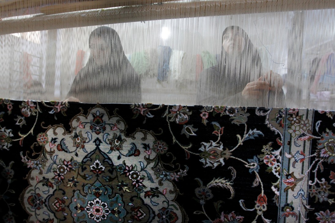 Loom workers weaving intricate patterns on a traditional carpet loom in Kashan, Iran.