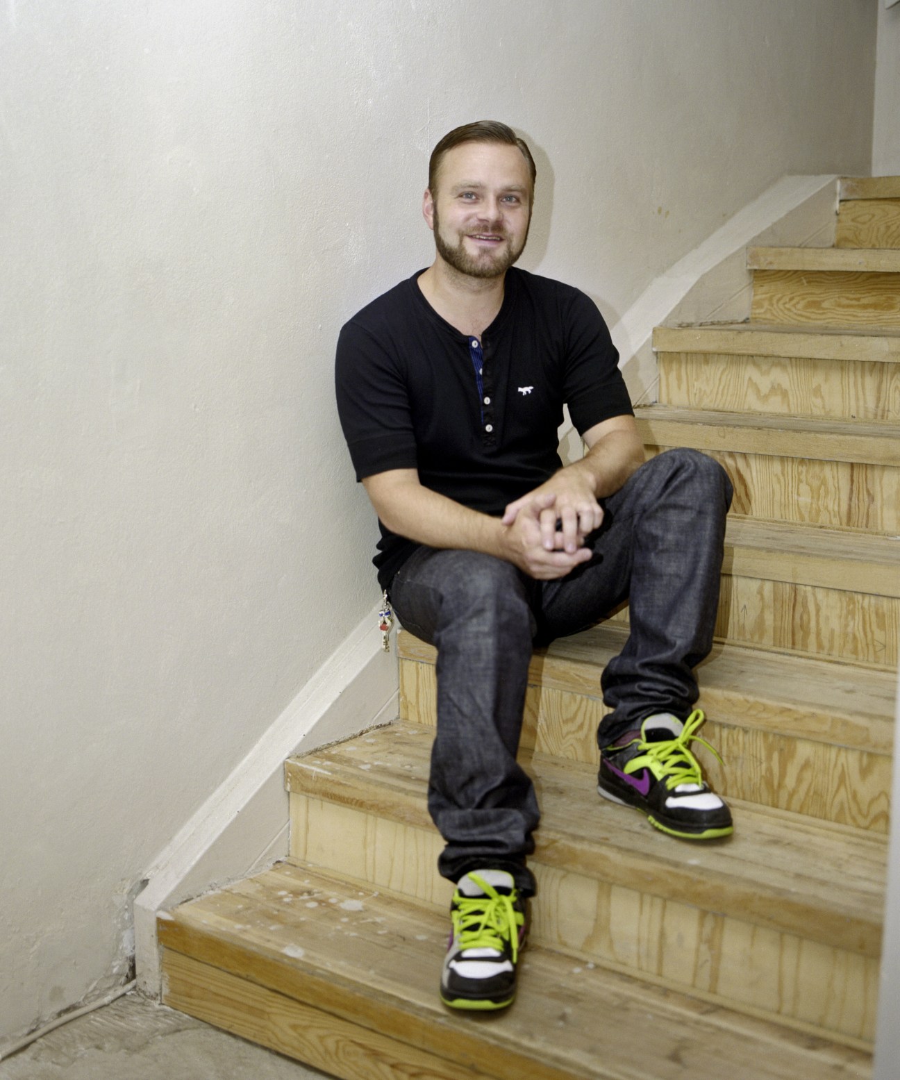 Man sitting on wooden stairs wearing black henley shirt and colorful sneakers