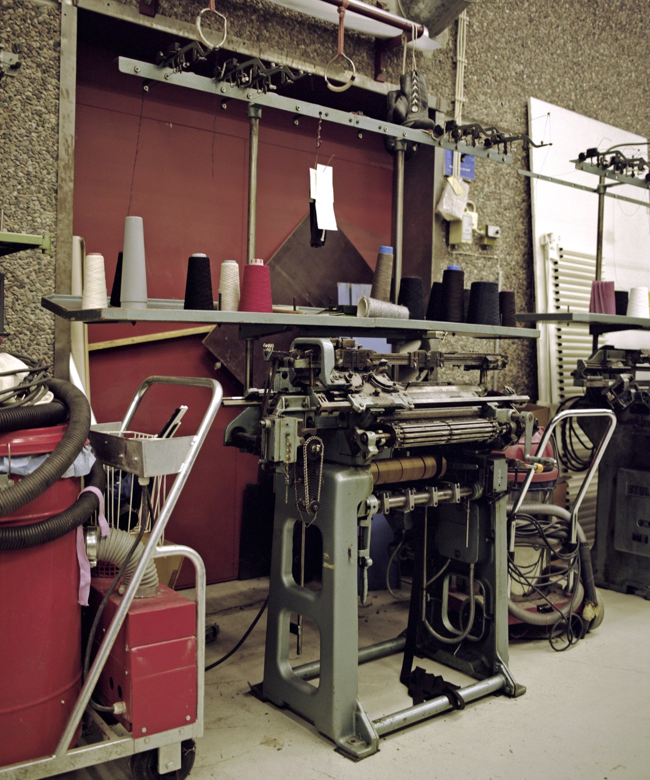 Industrial knitting machine with spools of colored yarn on shelf in factory workshop
