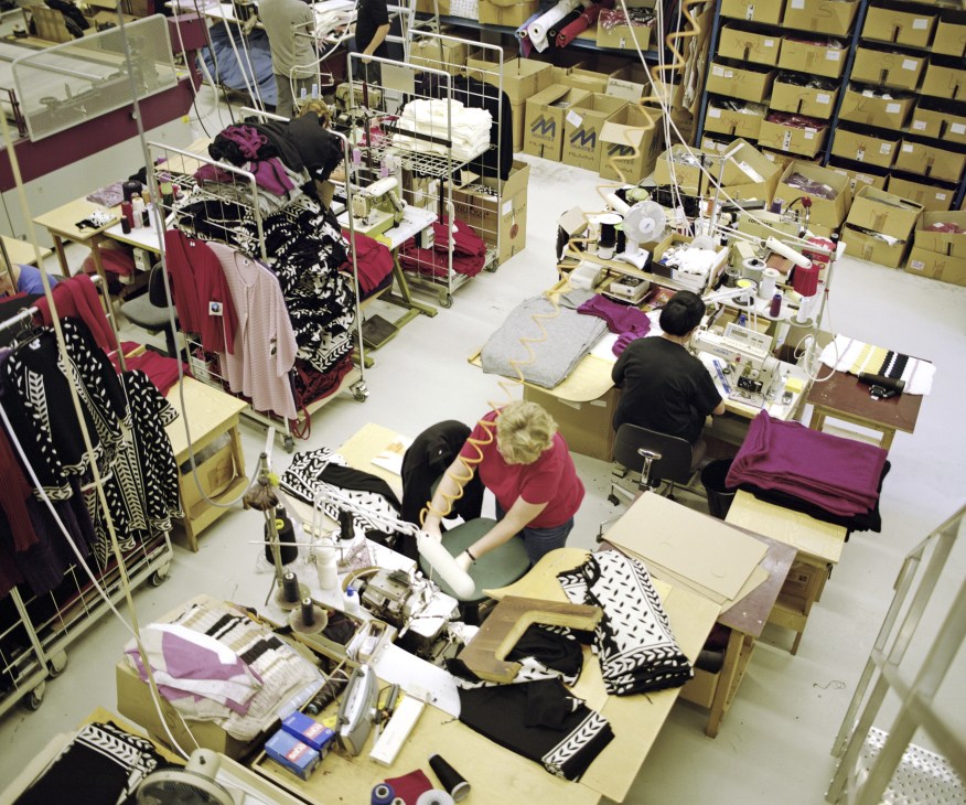Overhead view of Tuusula knitting factory with workers at tables assembling clothing items in magenta and black fabrics.