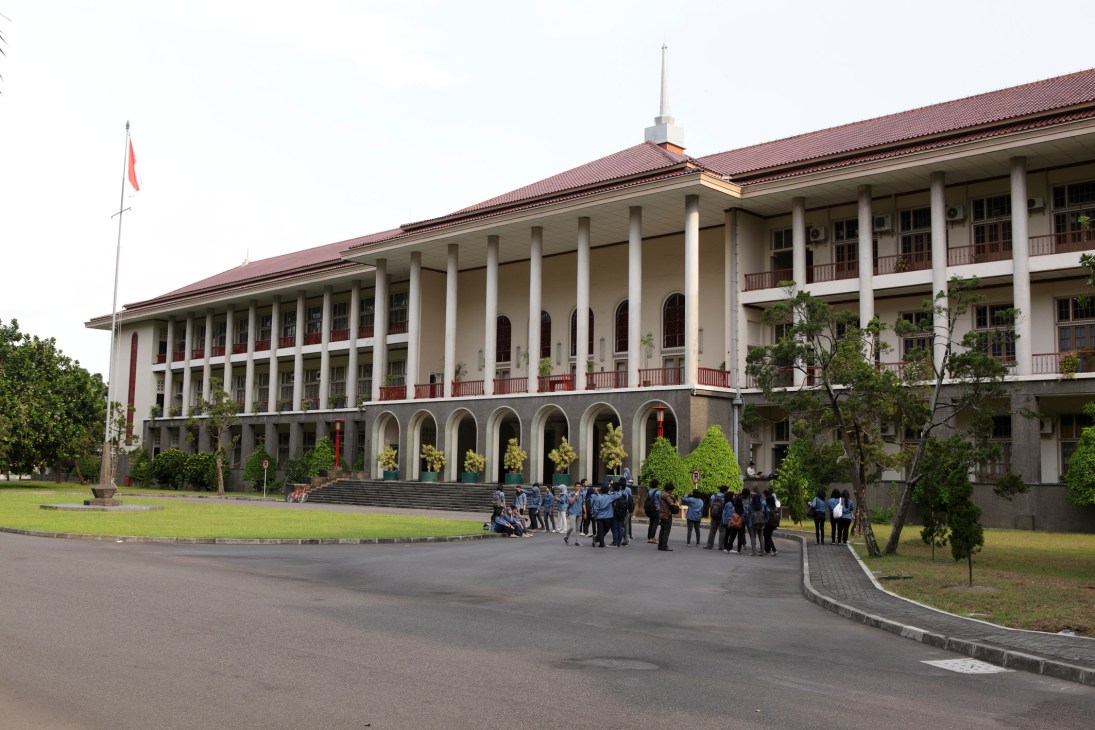 Entrance to one of the schools at Gadjah Mada University campus with classical colonial architecture and students gathered outside.