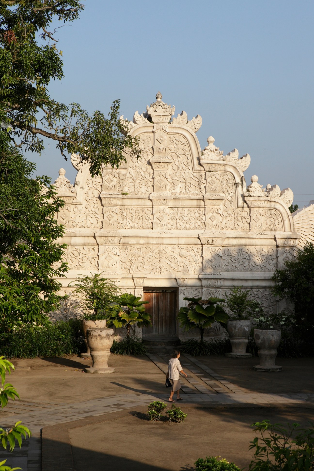 Ornately carved stone gateway at Taman Sari water palace with a person walking in the courtyard.